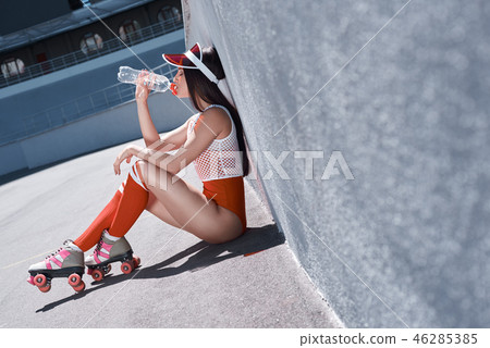 Young woman on roller skates and helmet drinking water. Stylish beautiful girl in shorts and a 46285385