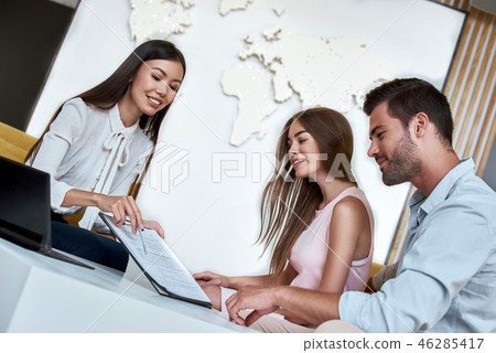 Couple sitting with manager at the travel agency office and reviewing contract Couple sitting with manager at the travel agency office and reviewing contract 46285417