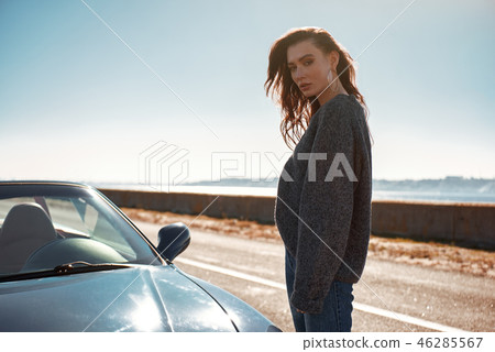 Young woman standing near roofless car outdoors on sunny day near the road Young woman standing near roofless car outdoors on sunny day near the road 46285567