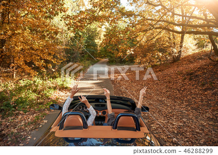 Female friends driving cabriolet with the hands up and having fun Female friends driving cabriolet with the hands up and having fun 46288299