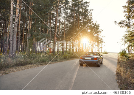 A black roofless car driving fast on the asphalt with a beautiful sunrise A black roofless car driving fast on the asphalt with a beautiful sunrise 46288366