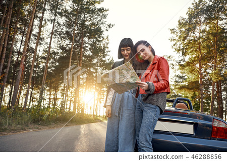 Two women trying to find the way on map near cabriolet Two women trying to find the way on map near cabriolet 46288856