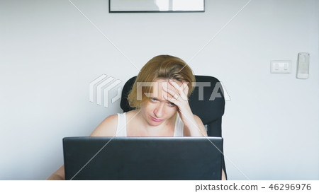 A woman using her laptop, sitting at the table, angry and irritated, swears. Human emotions A woman using her laptop, sitting at the table, angry and irritated, swears. Human emotions 46296976