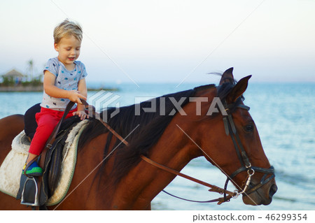 Cute little boy rides a horse on the beach. Copy space Cute little boy rides a horse on the beach. Copy space 46299354