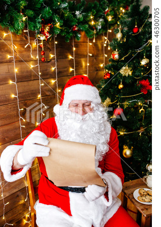 Portrait of Santa Claus sitting at his room at home near Christmas tree and big sack and reading 46300705