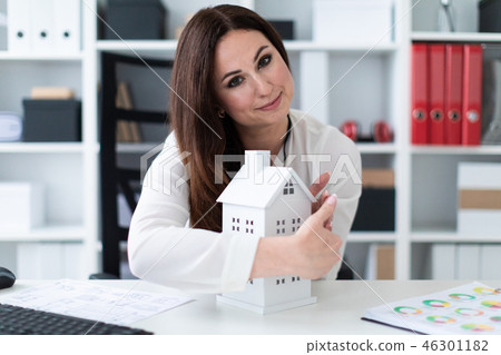 Young girl sitting at the table and holding hands near the layout of the house. Young girl sitting at the table and holding hands near the layout of the house. 46301182