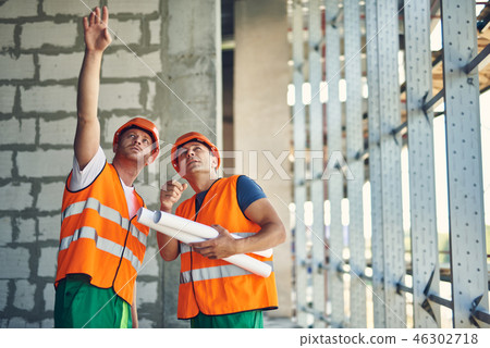 Thoughtful builder pointing to the ceiling while standing with coworker 46302718