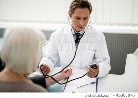 Calm doctor looking at the gauge and measuring blood pressure 46303070