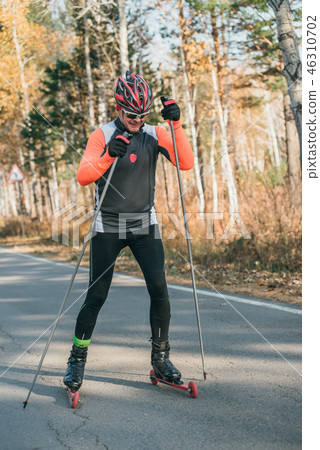 Training an athlete on the roller skaters. Biathlon ride on the roller skis with ski poles, in the Training an athlete on the roller skaters. Biathlon ride on the roller skis with ski poles, in the 46310702