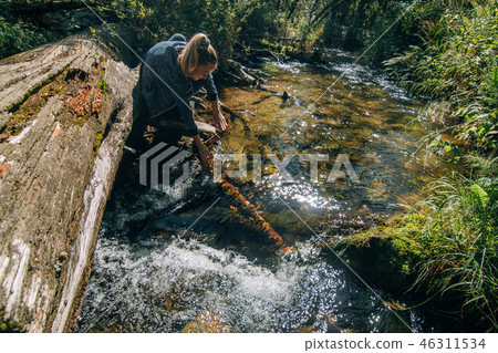Beautiful girl drinking water from river on log after travel. Woman traveler in summer passes on 46311534