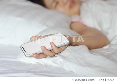 Woman sleeping in bed and holding a cell phone. Woman sleeping in bed and holding a cell phone. 46318092