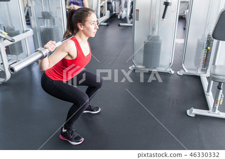 Beautiful girl exercising squatting with barbell 46330332