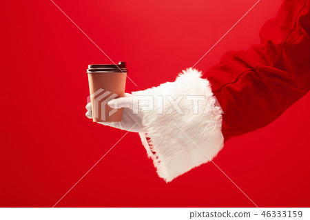Christmas coffee. The Santa hand holding cup of cofee isolated on a red background with space for 46333159