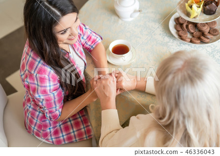 Elderly mother and her daughter holding hands while sitting at the table 46336043