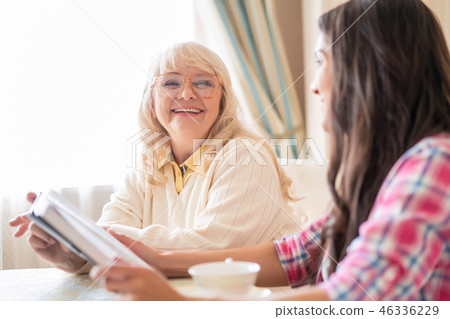 Senior mother and daughter read a book over a cup of tea Senior mother and daughter read a book over a cup of tea 46336229