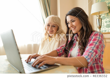 Woman types on the laptop while sitting with her senior mother. Woman types on the laptop while sitting with her senior mother. 46336332