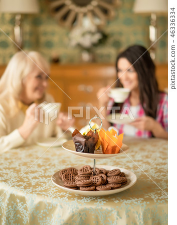 Senior mother drinks tea with her smiling daughter. Desserts stand on the table Senior mother drinks tea with her smiling daughter. Desserts stand on the table 46336334