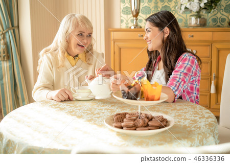 Senior mother drinks tea with her smiling daughter. Desserts stand on the table Senior mother drinks tea with her smiling daughter. Desserts stand on the table 46336336