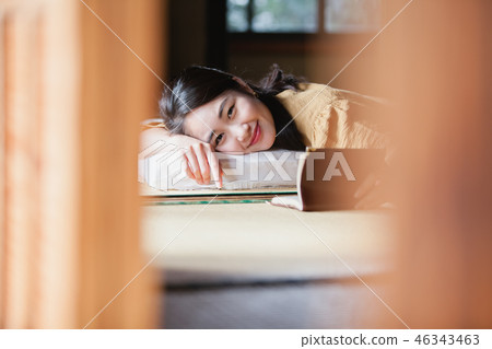 Young woman reading a book lying on tatami at travel destination Young woman reading a book lying on tatami at travel destination 46343463
