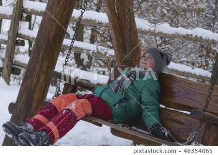 Boy riding a wooden swing on a background of snow Boy riding a wooden swing on a background of snow 46354065