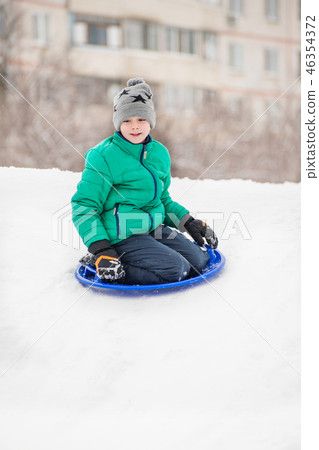 Boy slides down the hill on snow saucer 46354372