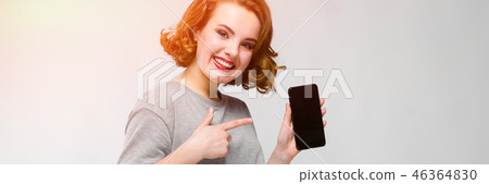 Charming young girl in a gray T-shirt on a gray background. A girl is holding a phone in her hand 46364830