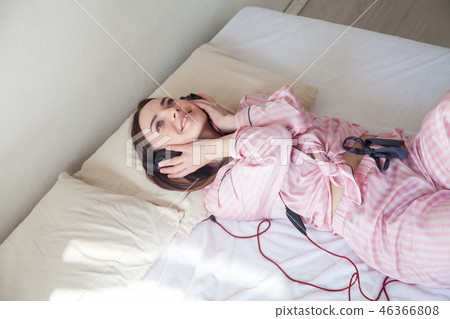 woman in pajamas on the bed listening to music headphones 46366808