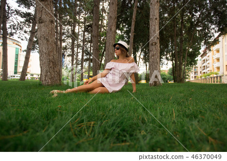 Beautiful girl in dress and hat in the park. Green grass and sunny. Background of trees Beautiful girl in dress and hat in the park. Green grass and sunny. Background of trees 46370049