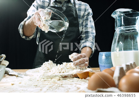 Professional male cook sprinkles dough with flour, preapares or bakes bread at kitchen table Professional male cook sprinkles dough with flour, preapares or bakes bread at kitchen table 46398655