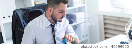 A man is sitting at a table in the office, working with documents and opening a bottle of water. 46399600