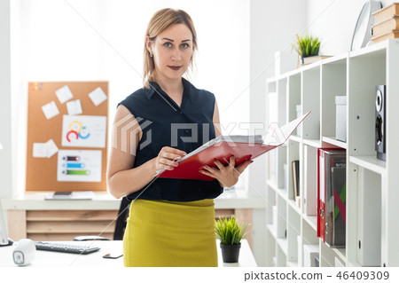 A young girl standing in the office and holding a folder with documents. 46409309