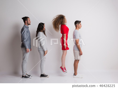 Side view of young group of friends standing in a studio, one is jumping. Side view of young group of friends standing in a studio, one is jumping. 46428225