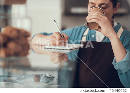 Calm barista drinking coffee and making notes in notebook Calm barista drinking coffee and making notes in notebook 46440662
