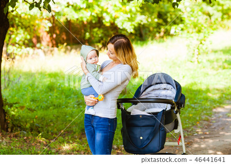 Side view of mother holding baby standing near stroller Side view of mother holding baby standing near stroller 46441641