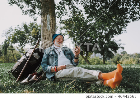 Senior man sitting on grass and looking at phone 46442563