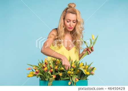 Happy beautiful blonde caucasian woman with big box of tulips on blue background. Happy beautiful blonde caucasian woman with big box of tulips on blue background. 46450429