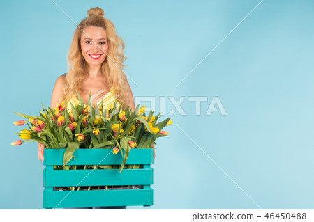 Happy caucasian blonde woman florist laughing and holding big box of tulips on blue background with 46450488