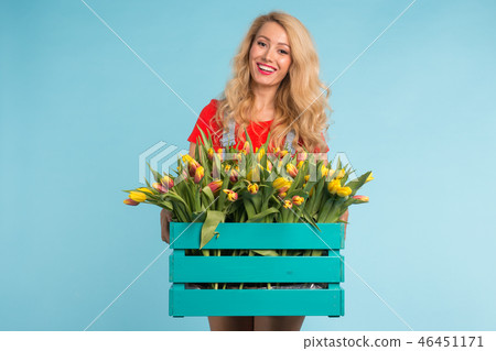 Happy caucasian blonde woman florist laughing and holding big box of tulips on blue background Happy caucasian blonde woman florist laughing and holding big box of tulips on blue background 46451171