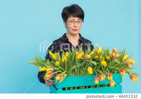Middle-aged female florist holding blue wooden box of tulips in studio 46451332