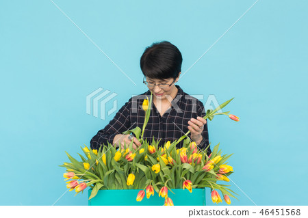 Middle-aged woman florist with wooden box of tulips on blue background 46451568