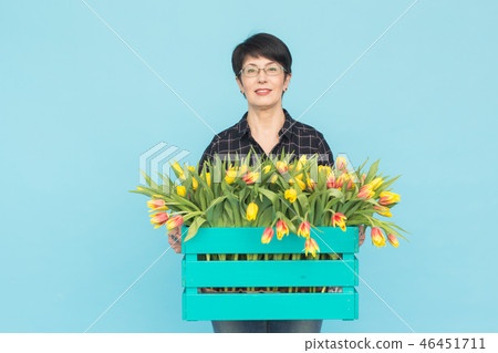 Middle-aged female florist holding blue wooden box of tulips in studio 46451711