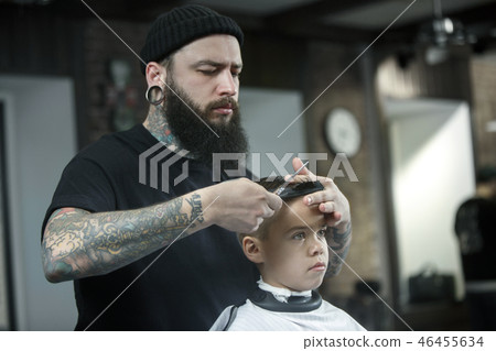 Children hairdresser cutting little boy against a dark background. Children hairdresser cutting little boy against a dark background. 46455634