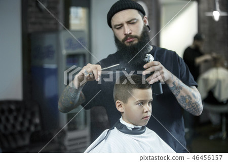 Children hairdresser cutting little boy against a dark background. Children hairdresser cutting little boy against a dark background. 46456157