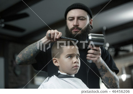 Children hairdresser cutting little boy against a dark background. Children hairdresser cutting little boy against a dark background. 46456206