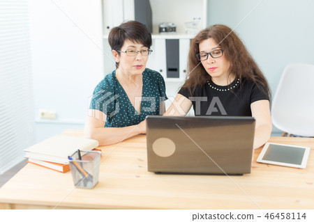 Business, technology and people concept - two women discuss a project watching in laptop Business, technology and people concept - two women discuss a project watching in laptop 46458114