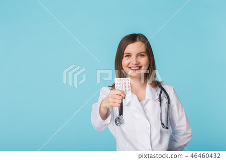 Attractive female doctor showing pink pills. Beautiful young physician holding medicaments over blue Attractive female doctor showing pink pills. Beautiful young physician holding medicaments over blue 46460432