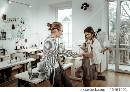 Tall handsome dressmaker in eyeglasses checking up a new dress Tall handsome dressmaker in eyeglasses checking up a new dress 46461401