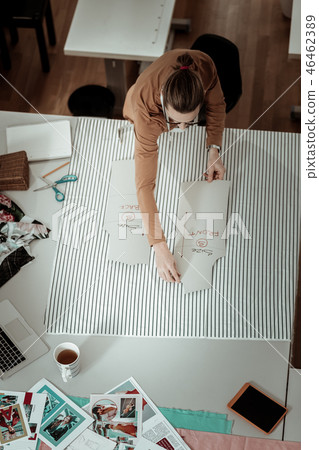 Tall fair-haired designer in a brown garment working with patterns Tall fair-haired designer in a brown garment working with patterns 46462389