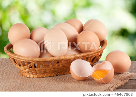 eggs in a wicker basket on a wooden board with blurred garden background 46467808