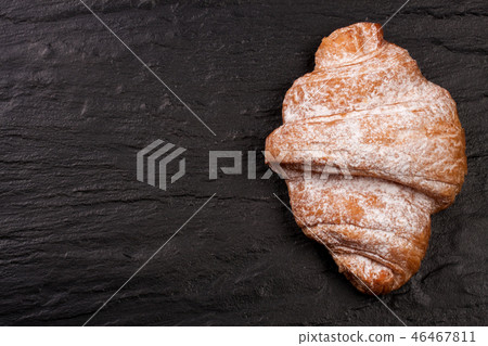 one croissant sprinkled with powdered sugar on black stone background with copy space for your text 46467811